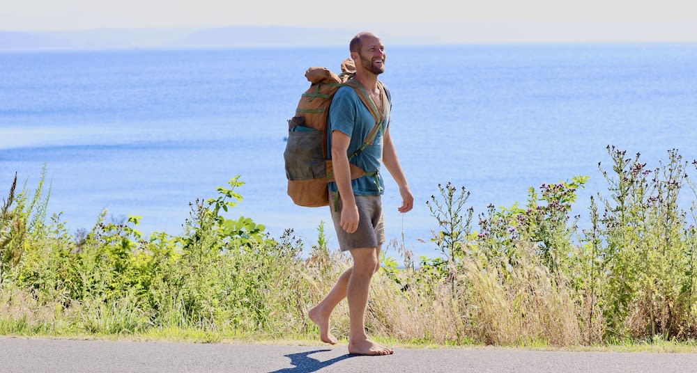 Robin Greenfield walking on the side of a road with his bag